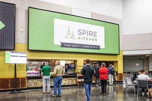 People queue at a food counter under a large sign reading "Spire Kitchen".