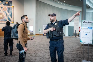 A public safety agent directs a man with a backpack in a conference hall. 