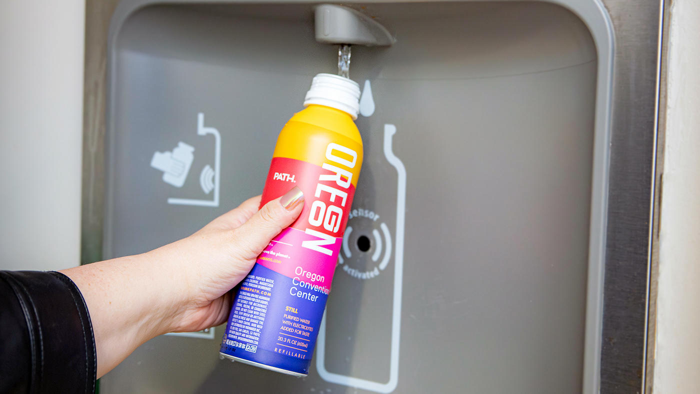 A hand holds a brightly colored metal bottle under a water spout