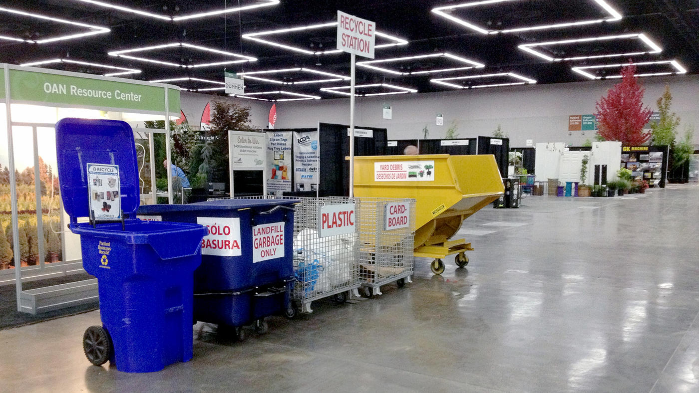A row of colorful recycling containers are neatly arranged and labeled inside a large exhibit hall