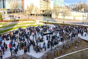 Large outdoor gathering with people mingling around tables.